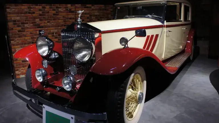 A cream and red Rolls Royce Phantom II displayed near a brick wall inside the Glion Museum in Osaka, Japan