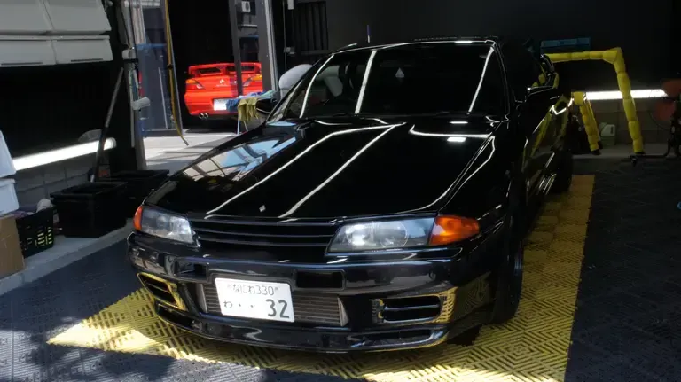 A black Nissan Skyline R32 GT-R parked in a dedicated space behind MR.HIRO car studio in Osaka, Japan