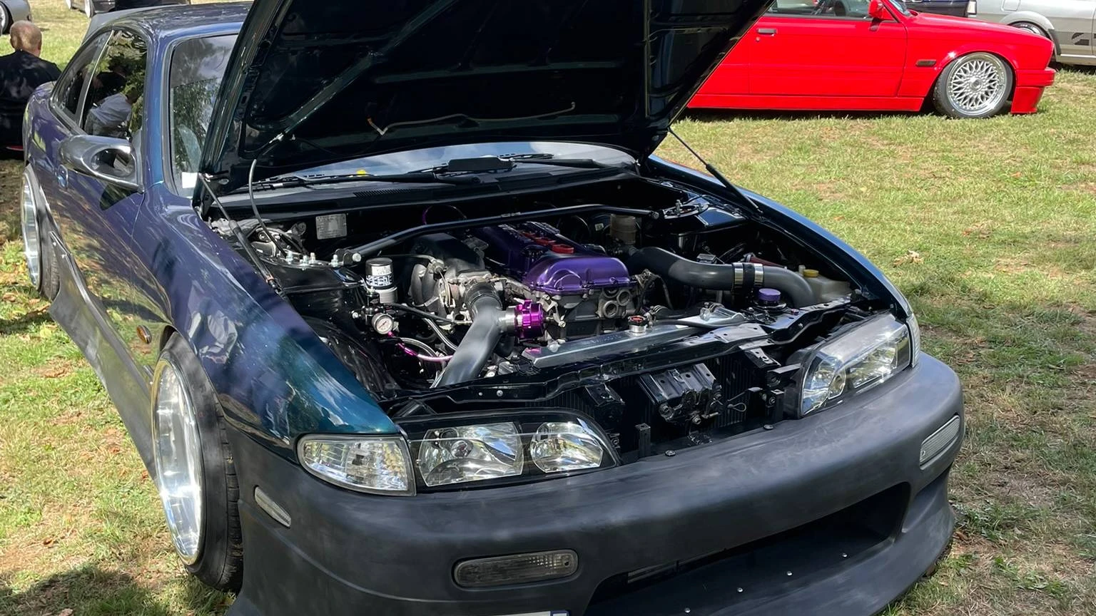 Front side view of a stanced blue 1997 Nissan 200SX S14 with an open hood