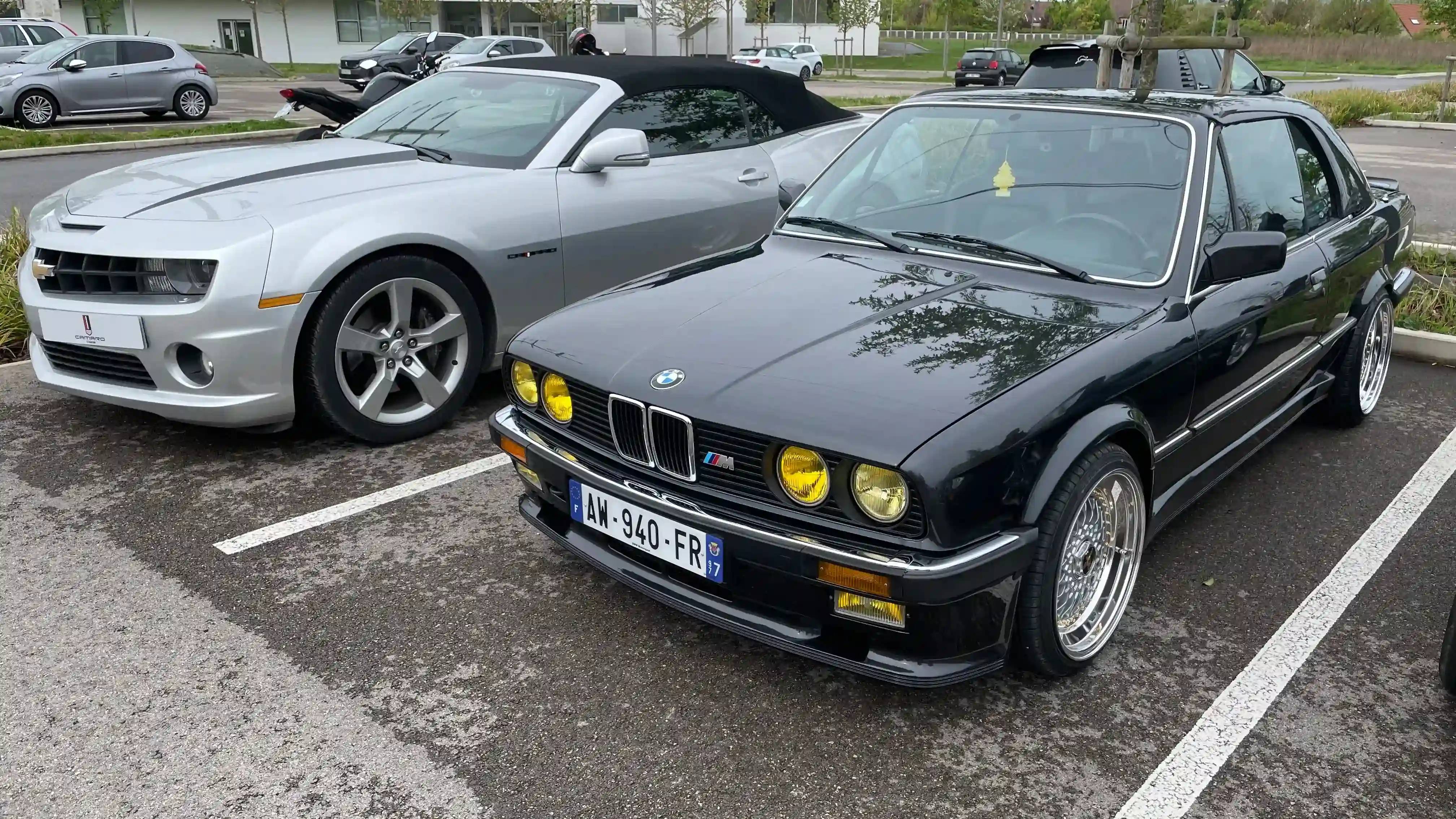 A grey convertible Chevrolet Camaro MK5 next to a black BMW M3 E30, both parked