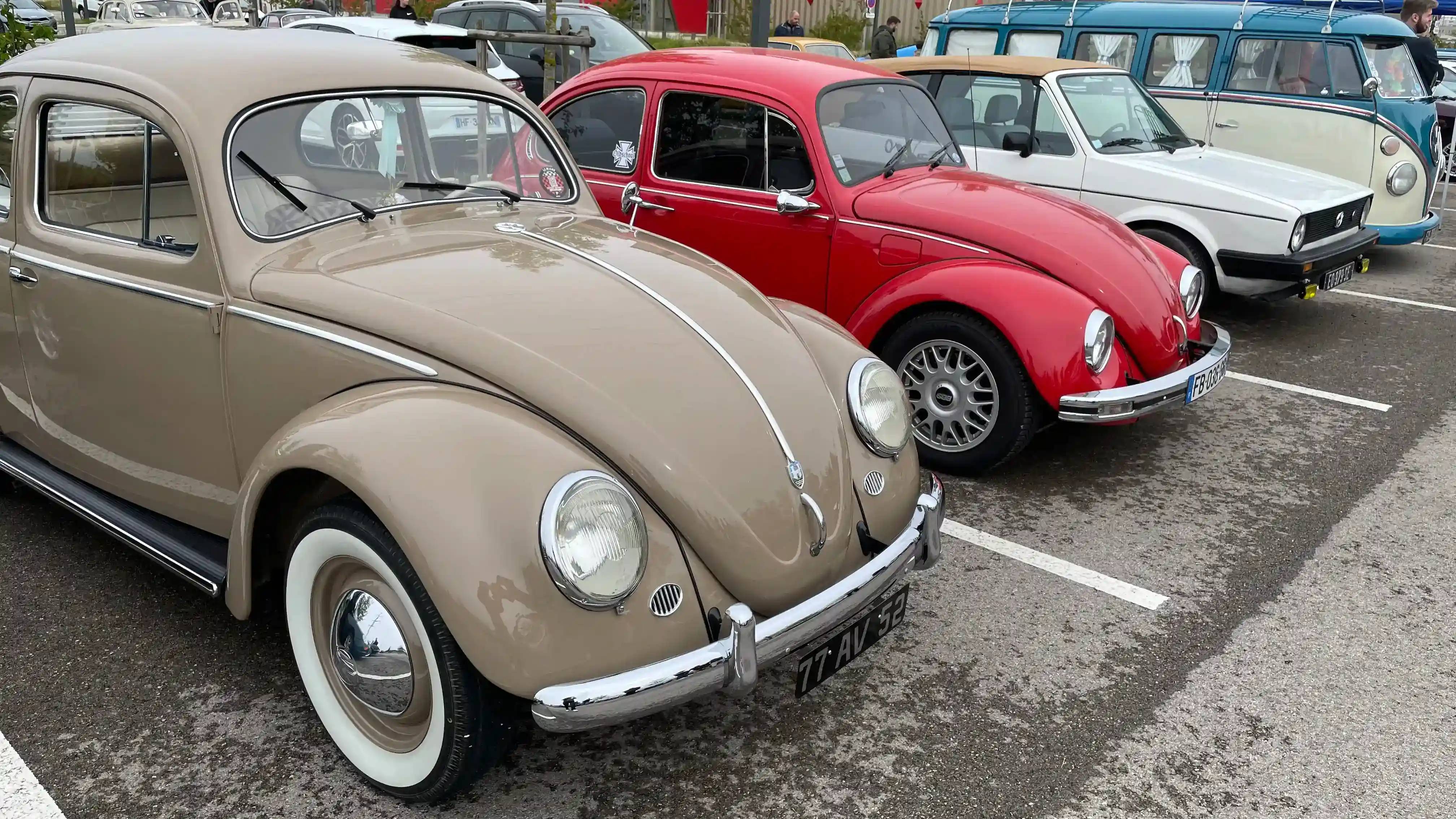 A light brown Volkswagen Beetle, a red Volkswagen Beetle, a white convertible Volkswagen Golf MK2, a white/blue Volkswagen Combi all parked