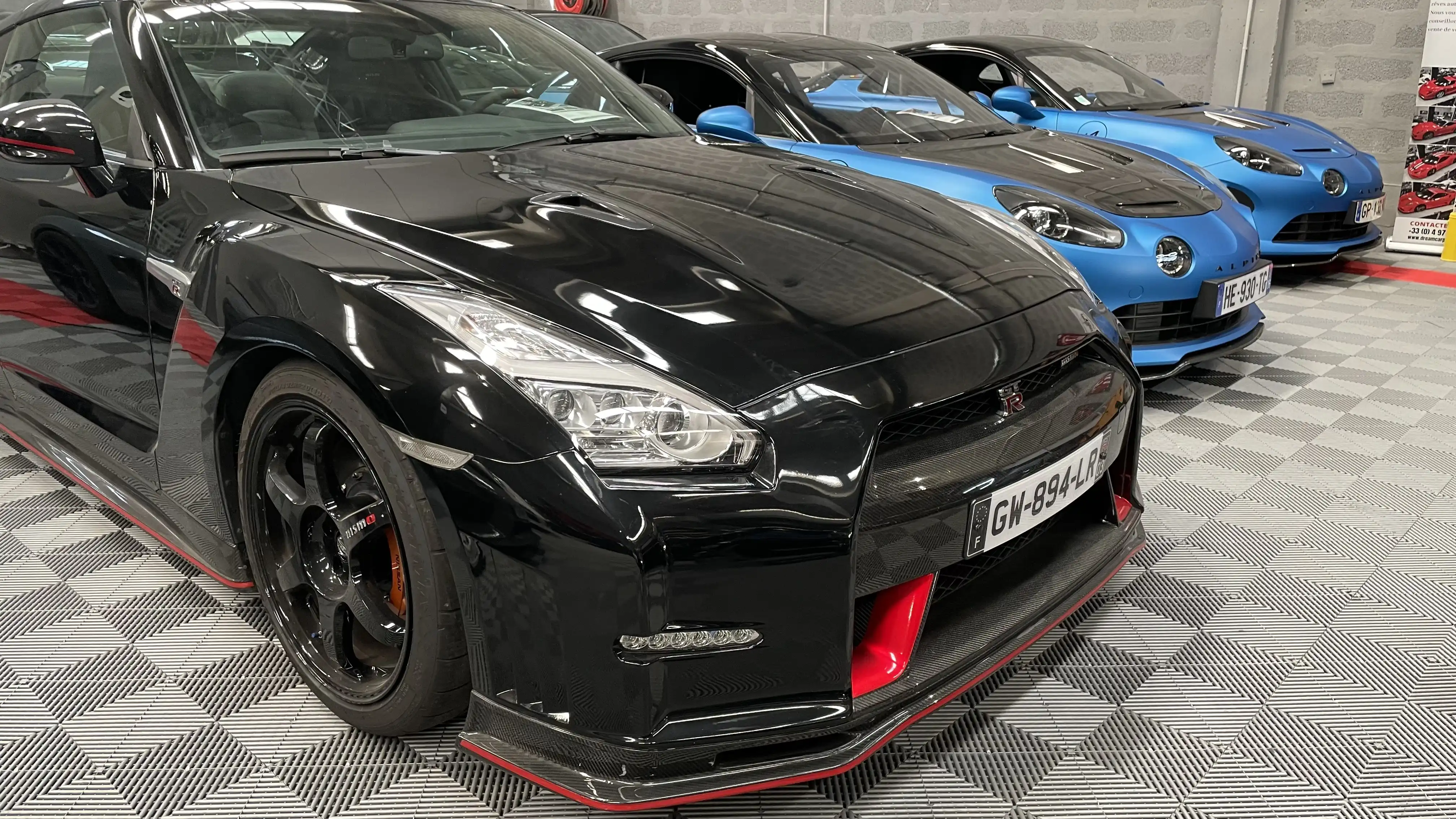 A black Nissan GT-R R35 Nismo next to two blue Alpine inside the showroom of Dream Car Performance