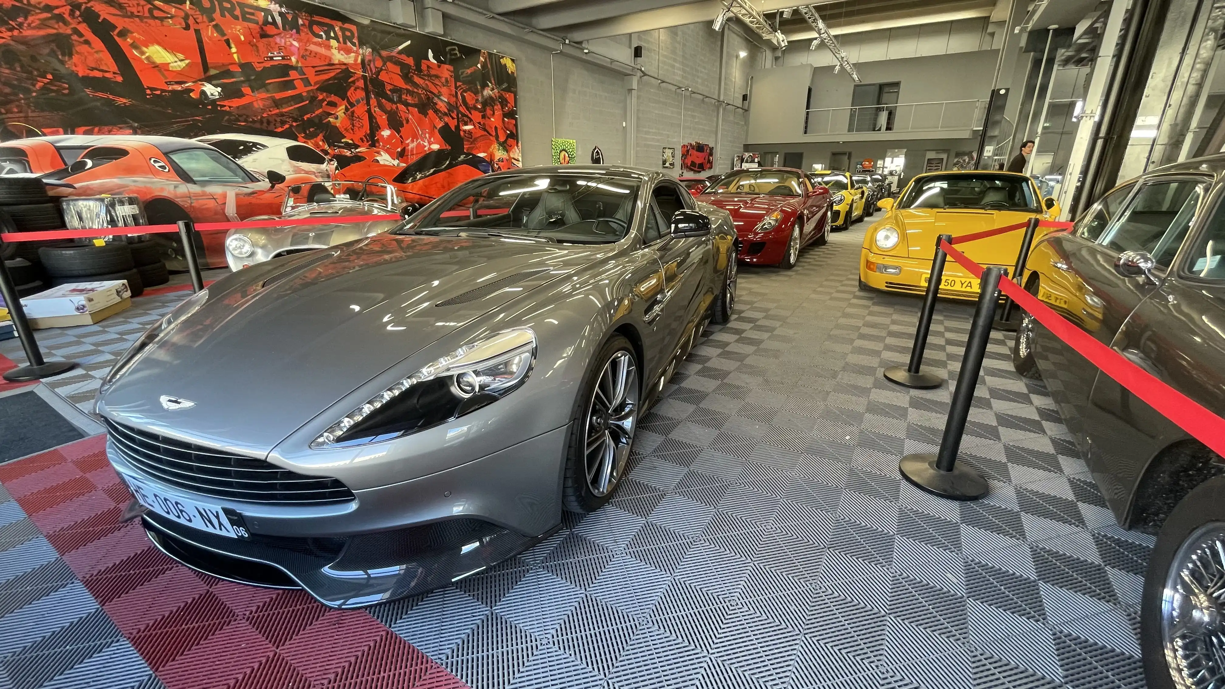 A grey Aston Martin Vanquish V12 in front of various luxury cars inside the showroom of Dream Car Performance